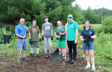 Four adults and two youth standing on a trail, holding rakes