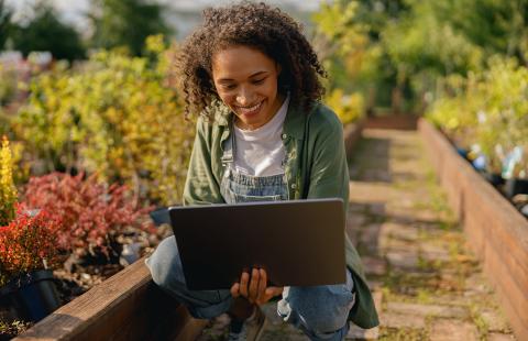 Woman in a garden of raised beds with a laptop - Adobe Stock ©Attasit