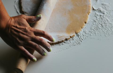 Person's hands rolling flour on dough with rolling pin