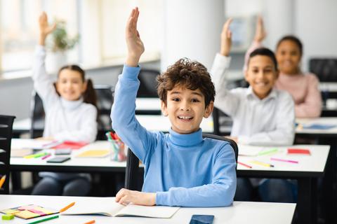 Children in classrrom raising hands